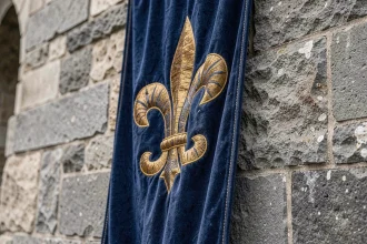 Drapeau royal français à fleurs de lys dorées sur velours bleu accroché à un mur de château en pierre ancienne