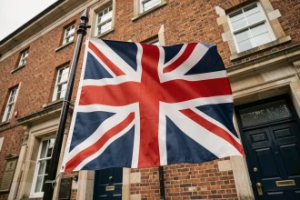 Drapeau Union Jack britannique flottant sur un mât en fer forgé devant un bâtiment en briques rouges typiquement anglais